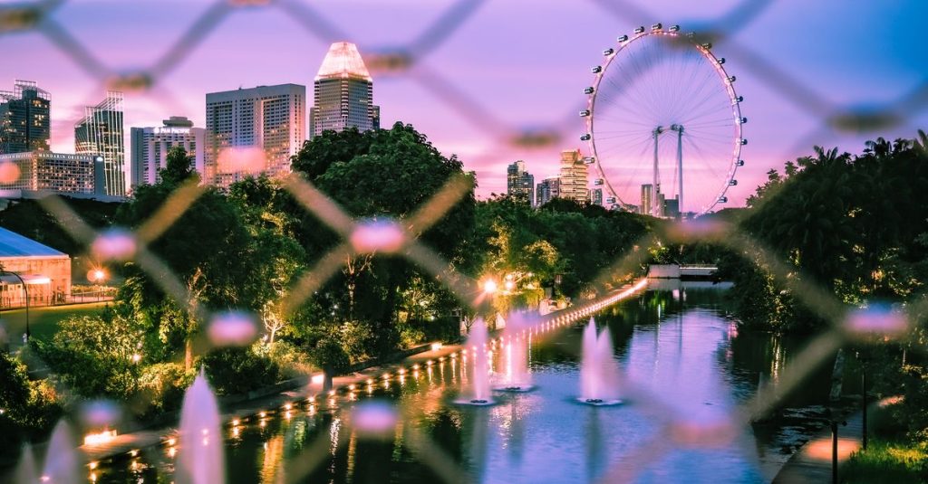 A beautiful skyline view of a city park with a Ferris wheel and fountains at dusk.